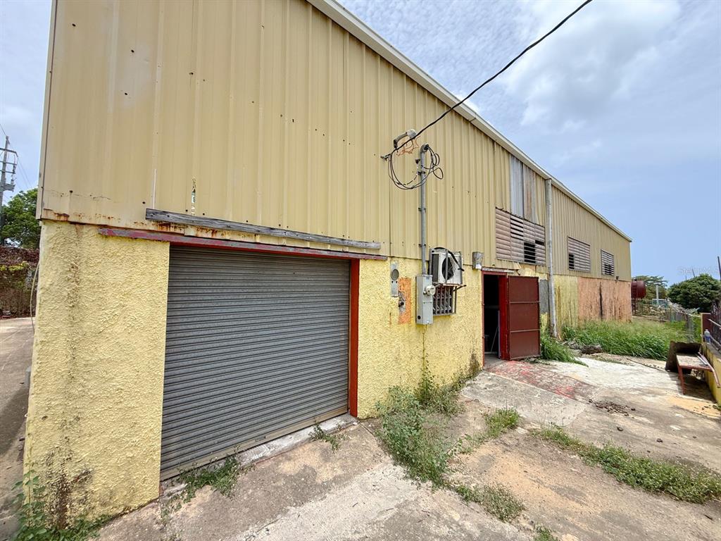 An exterior view of a yellow industrial building with a roll-up door and side entrance — KM 1.6 ROUTE 200, VIEQUES, PR