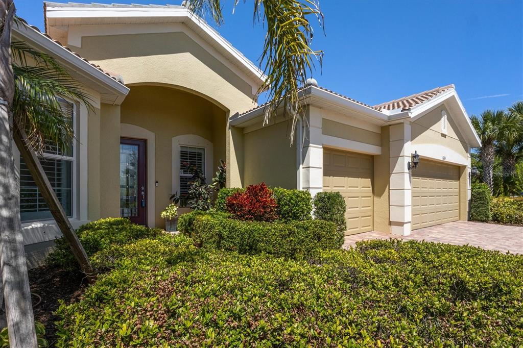 A single-story house with a tan stucco exterior, a two-car garage, and landscaped front bushes — 6124 ABACO DRIVE, SARASOTA, FL