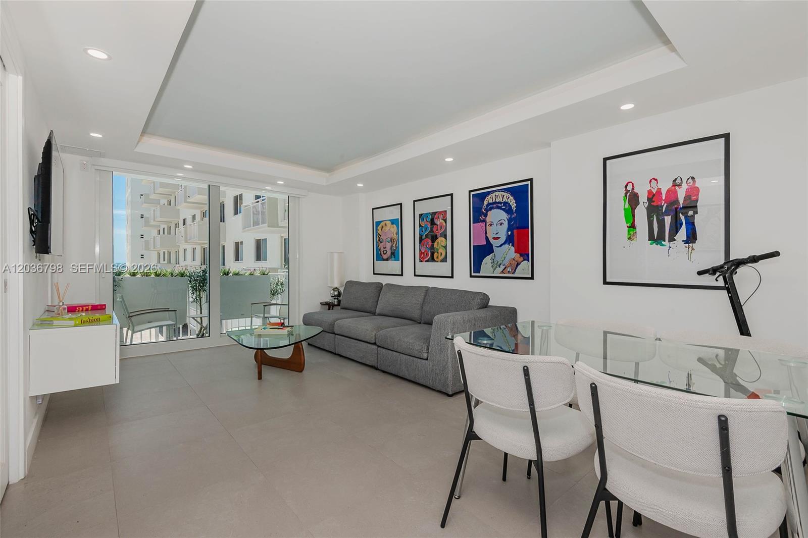 A modern living and dining area features a gray sofa, glass tables, and pop art — 345 Ocean Dr # 326, Miami Beach FL 33139, MIAMI BEACH, FL