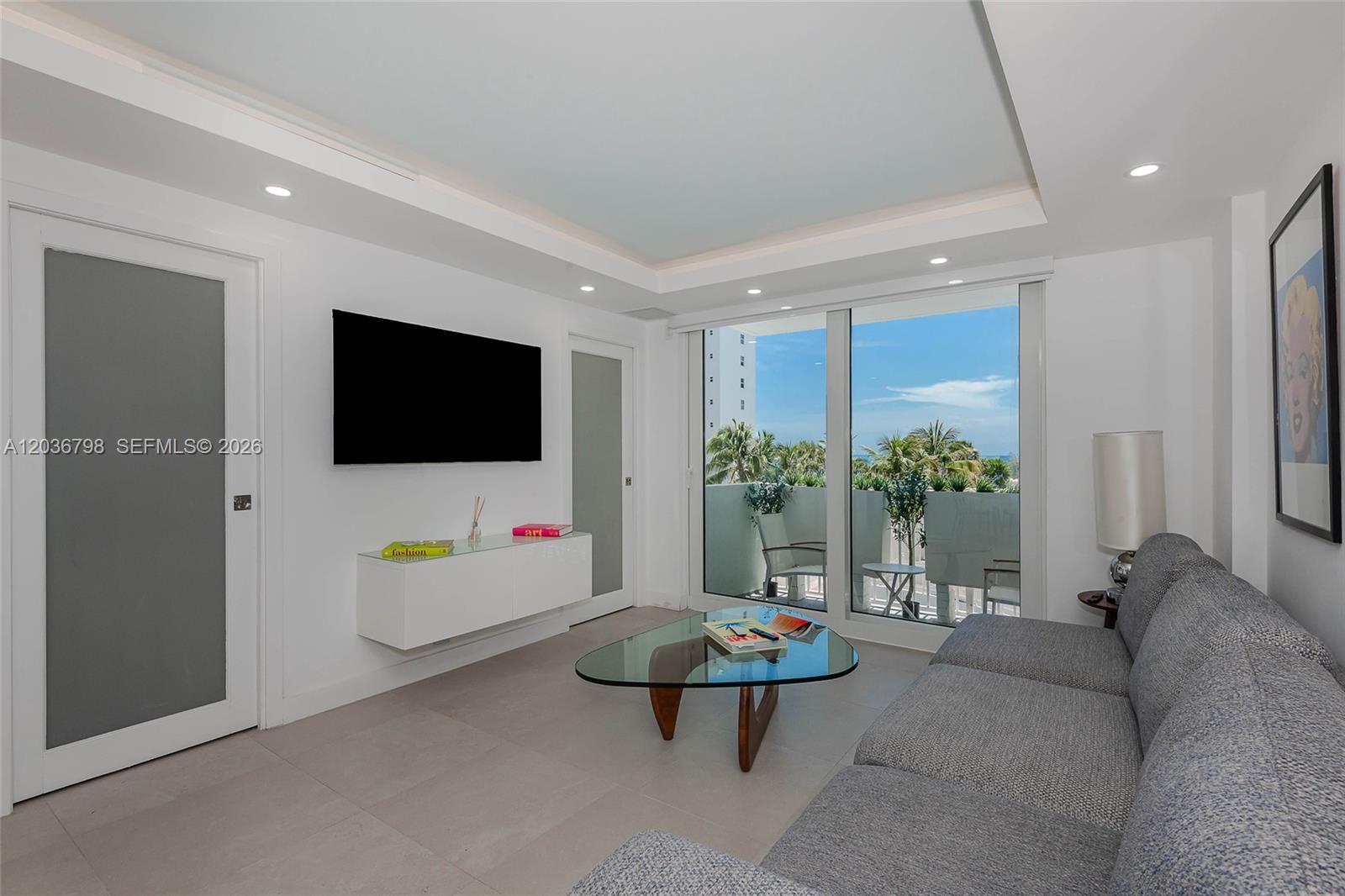 A modern living room features a grey sofa, glass coffee table, and a balcony view — 345 Ocean Dr # 326, Miami Beach FL 33139, MIAMI BEACH, FL