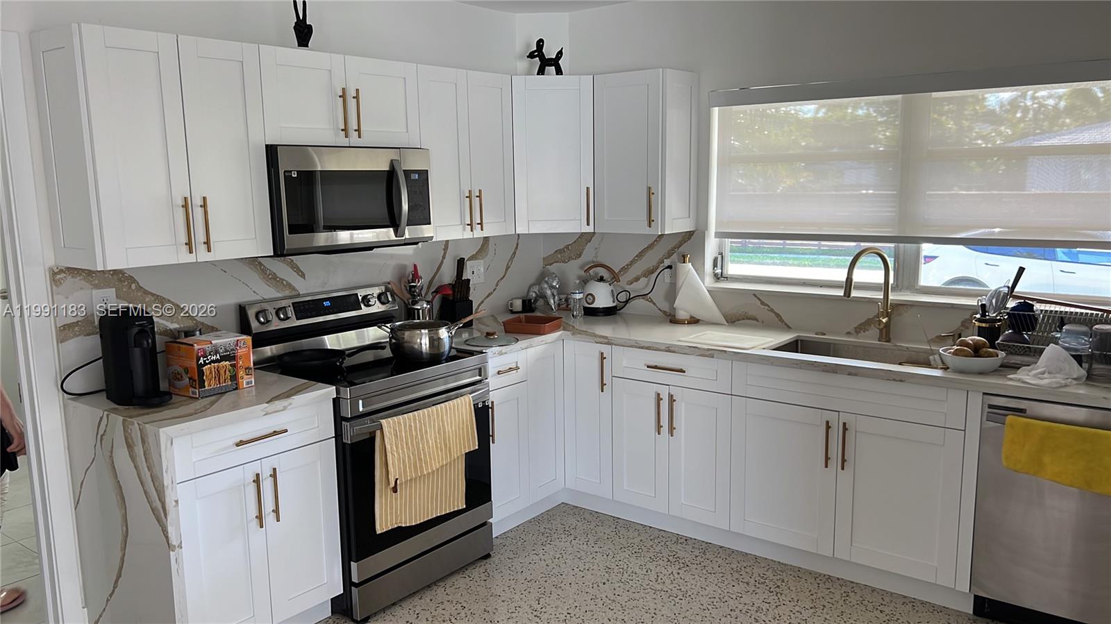 A kitchen features white shaker cabinets, gold hardware, stainless steel appliances, and marble-patterned countertops — 750 Polk St, Hollywood FL 33019, HOLLYWOOD, FL
