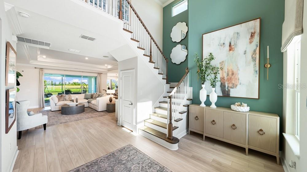 A bright entryway features a staircase, a teal accent wall with art, and light wood flooring — 16286 ALPHA GROVE PLACE, ODESSA, FL
