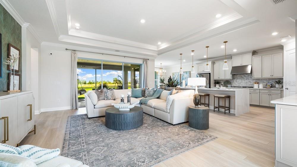 An open-concept living room and kitchen feature light wood floors, a sectional sofa, and cabinetry — 16286 ALPHA GROVE PLACE, ODESSA, FL