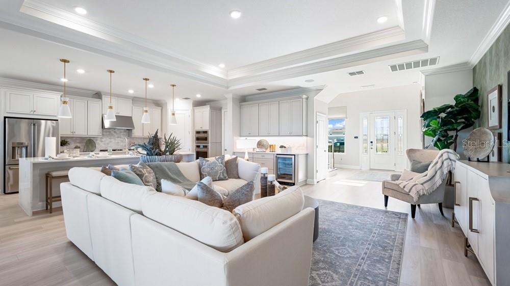 An open-concept living room and kitchen featuring white cabinetry, a large sofa, and light flooring — 16286 ALPHA GROVE PLACE, ODESSA, FL