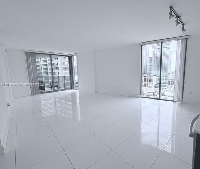 An empty living room features white tile flooring, white walls, and floor-to-ceiling windows with balcony access — 31 SE 6th St # 2001, Miami FL 33131, MIAMI, FL