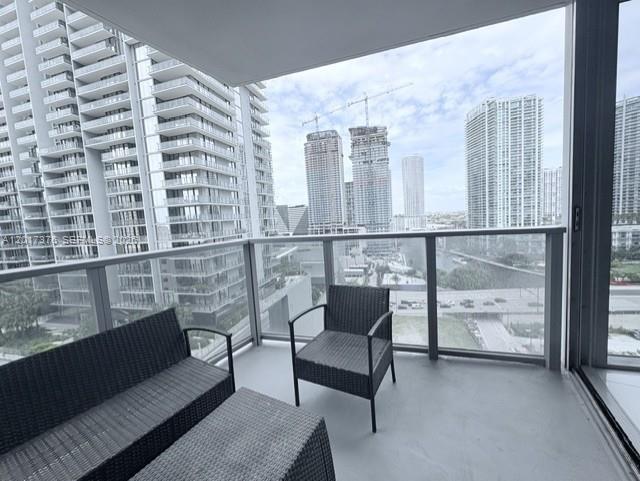 A balcony with wicker furniture overlooks a city skyline featuring several high-rise buildings and construction — 31 SE 6th St # 2001, Miami FL 33131, MIAMI, FL