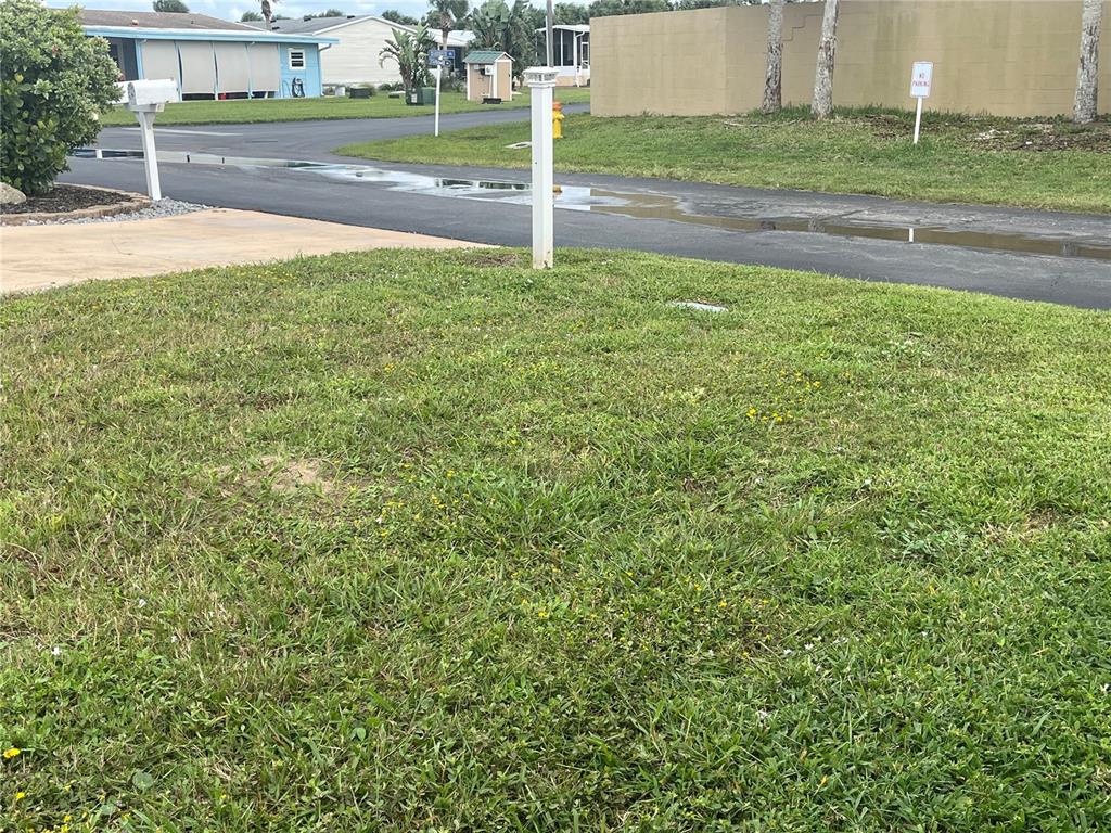 A grassy lawn sits in front of a paved road with puddles and a wall — 228 STARBOARD DRIVE, FLAGLER BEACH, FL