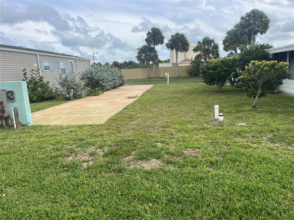 A grassy lot features a concrete driveway next to a mobile home and palm trees — 228 STARBOARD DRIVE, FLAGLER BEACH, FL