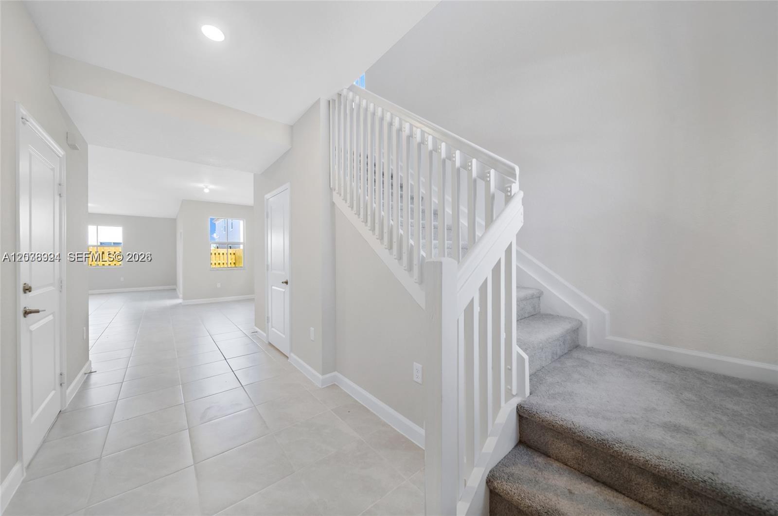 A bright entryway features light tile flooring, white walls, and a carpeted staircase with railings — 2373 NW 130th St, Miami FL 33167, MIAMI, FL