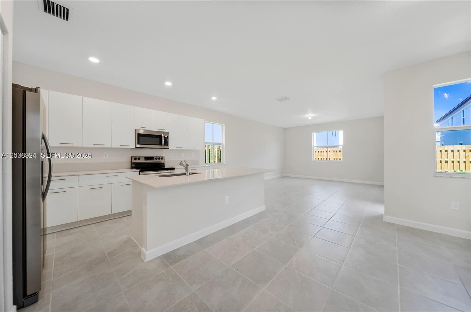 A modern kitchen with white cabinets and a quartz island opens into a living area — 2373 NW 130th St, Miami FL 33167, MIAMI, FL