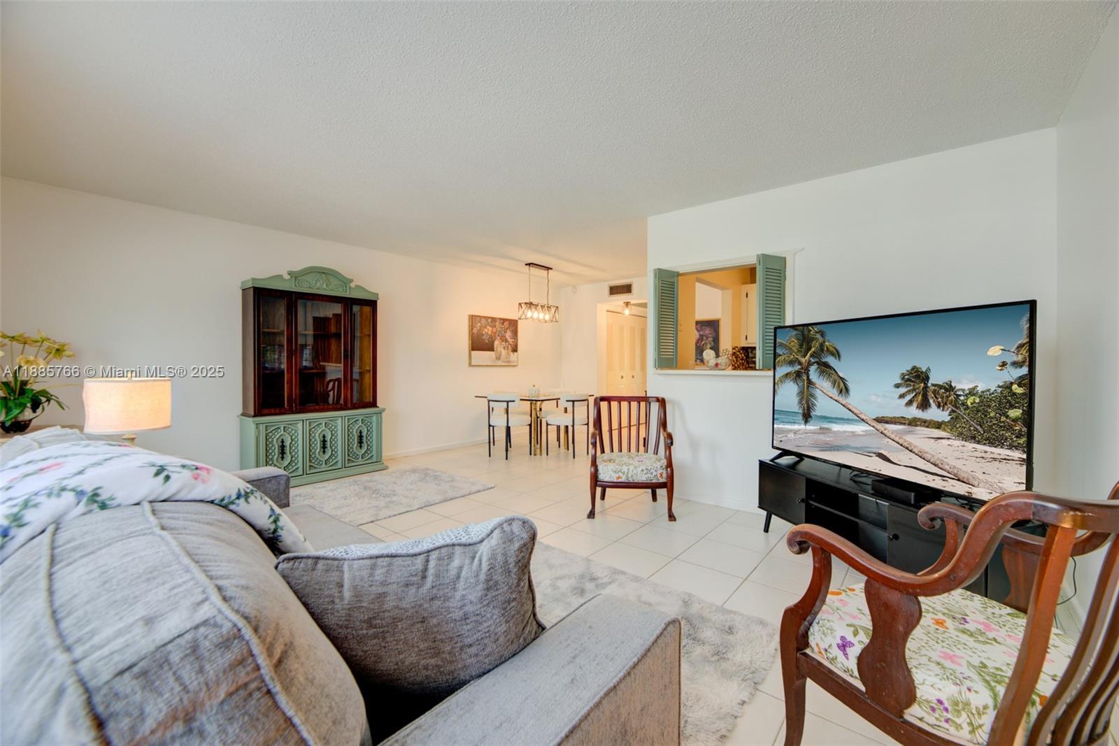A living room with tile floors, a television, and a dining area in the background — 2031 Durham B # 2031, Deerfield Beach FL 33442, DEERFIELD BEACH, FL