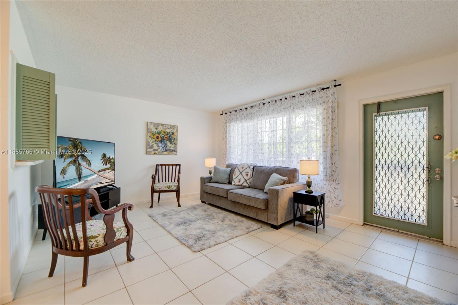 A living room features a gray sofa, two wooden chairs, a television, and tile flooring — 2031 Durham B # 2031, Deerfield Beach FL 33442, DEERFIELD BEACH, FL