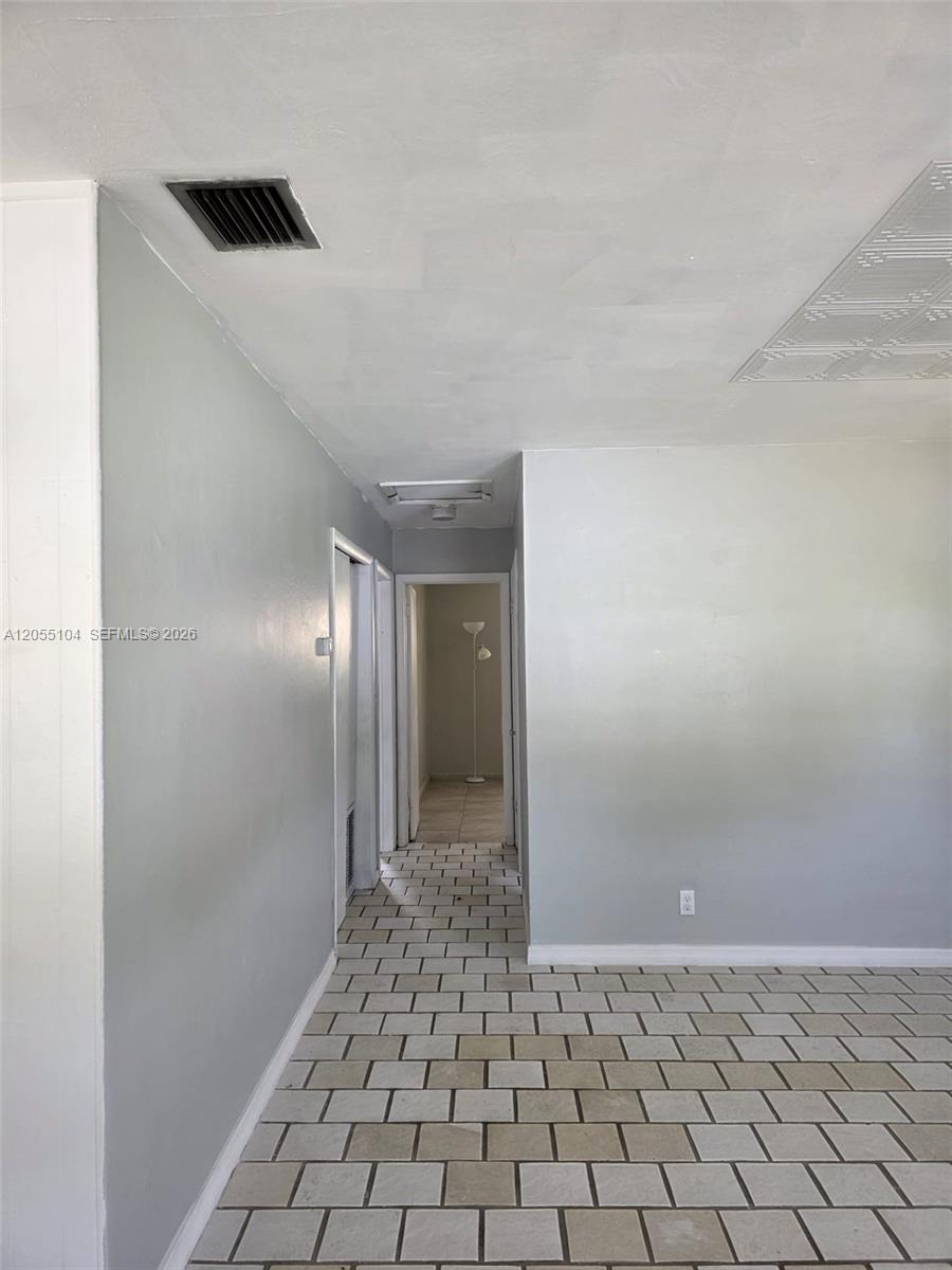 A hallway with light-colored tile flooring leads toward a doorway in a room with gray walls — 46 NW 14th Ct, Dania Beach FL 33004, DANIA BEACH, FL