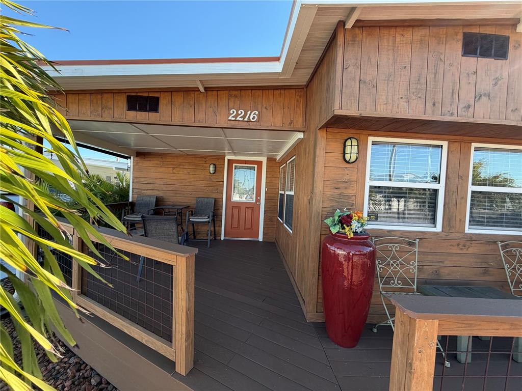 A wooden deck with a covered porch features a red door and outdoor seating — 2216 PENNSYLVANIA AVENUE, BRADENTON, FL