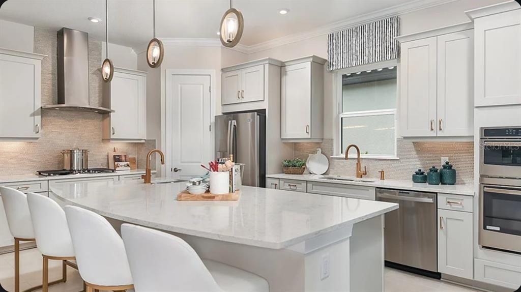 A modern kitchen features white cabinetry, a large quartz island, and stainless steel appliances — 3118 VICENZA COURT, BRADENTON, FL