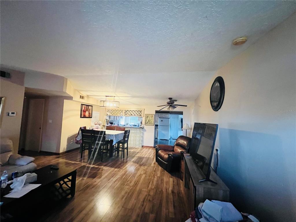 A living room and dining area with wood-look flooring, a ceiling fan, and kitchen access — 5543 MOOG ROAD, NEW PORT RICHEY, FL
