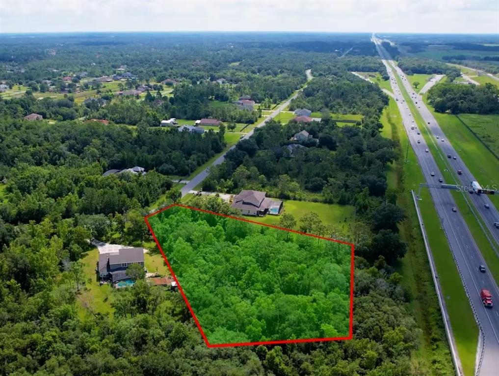 An aerial view shows a wooded residential lot outlined in red next to a highway — Lot 32 STARRY STREET, ORLANDO, FL