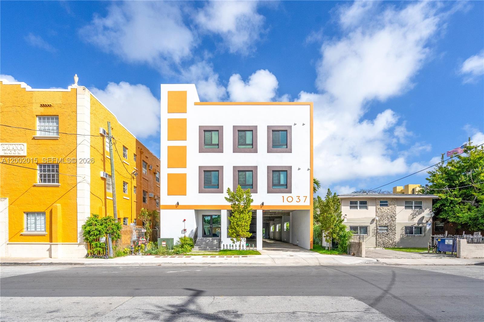 A modern three-story building with white and orange exterior walls stands between two older structures — 1037 NW 2nd St, Miami FL 33128, MIAMI, FL