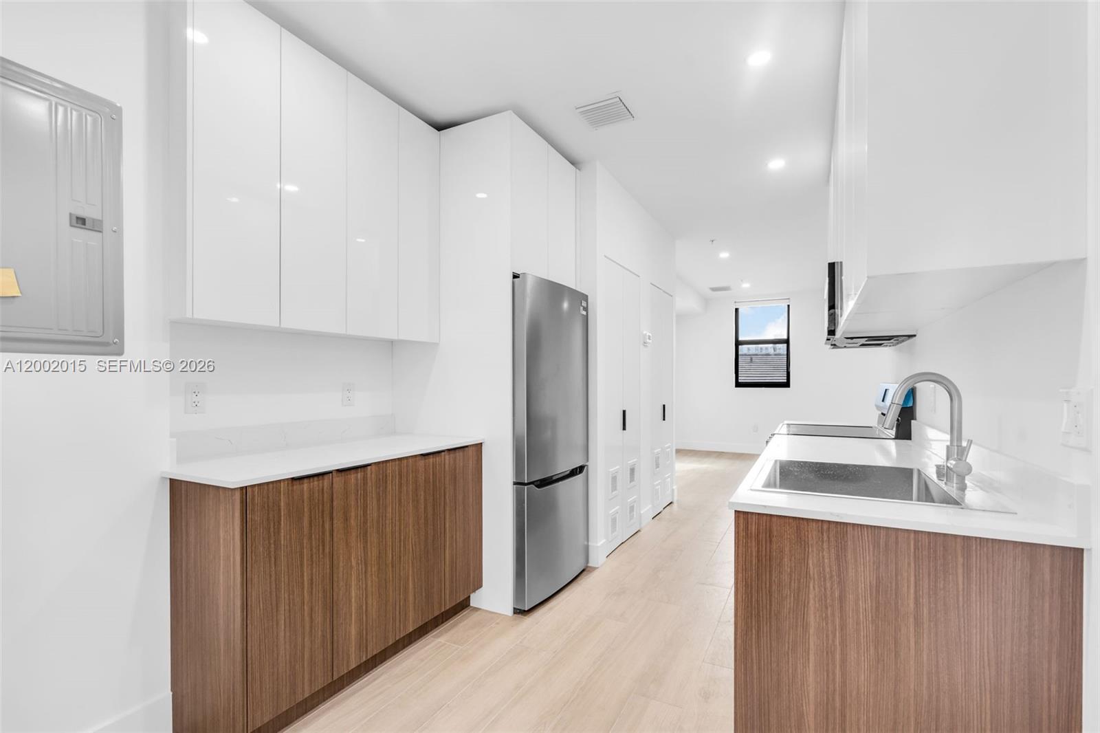 A modern kitchen features white upper cabinets, wood-grain lower cabinets, and stainless steel appliances — 1037 NW 2nd St, Miami FL 33128, MIAMI, FL