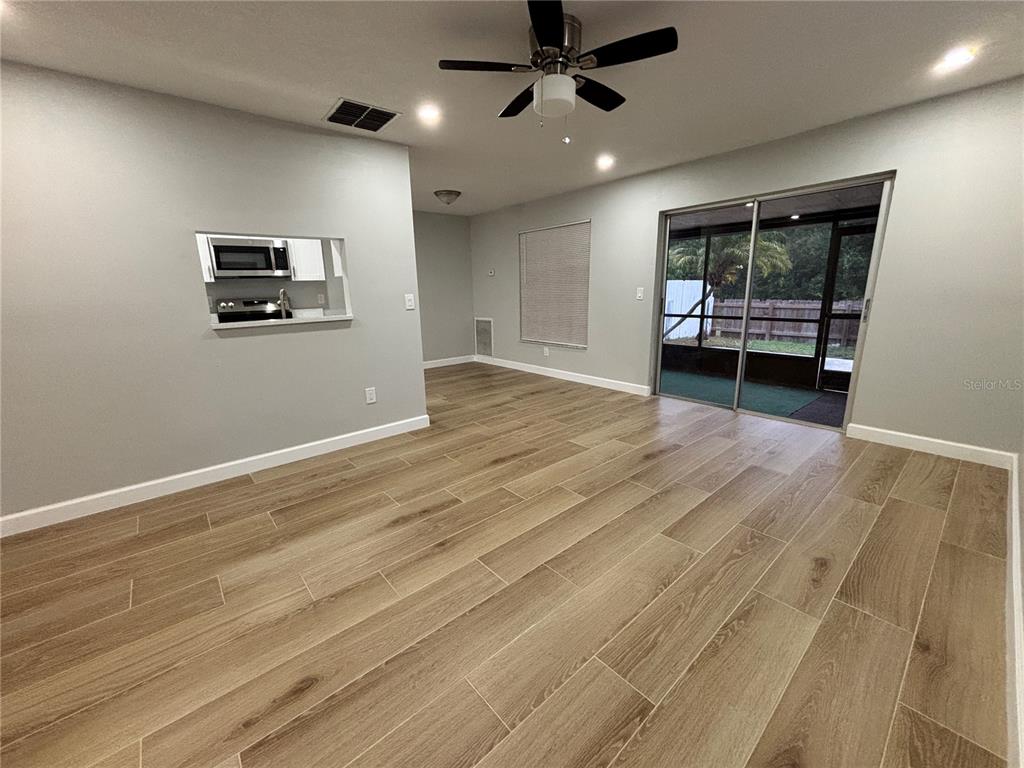 An open living area features wood-look tile flooring, a ceiling fan, and a sliding glass door — 14025 VILLAGE VIEW DRIVE, TAMPA, FL