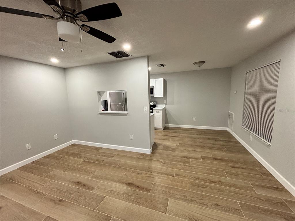 An interior view of a room with light gray walls, wood-look flooring, and a ceiling fan — 14025 VILLAGE VIEW DRIVE, TAMPA, FL