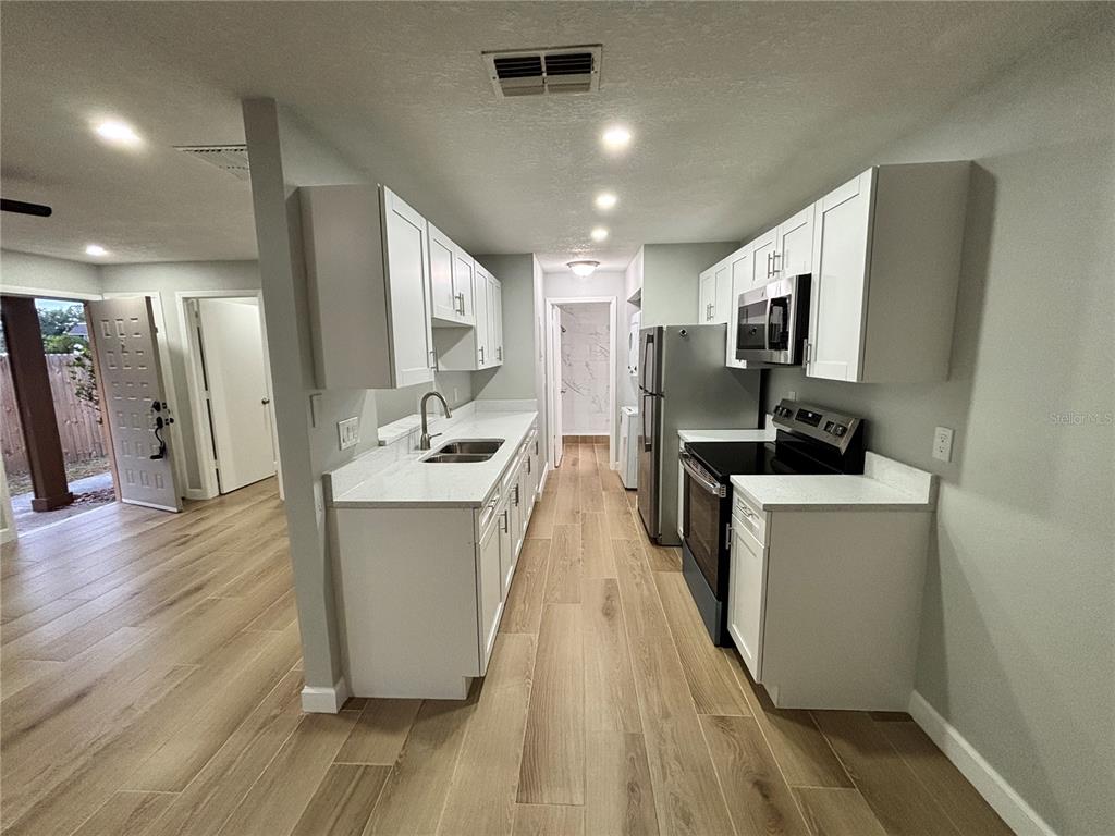 A galley kitchen features white cabinets, light countertops, stainless steel appliances, and wood-look tile flooring — 14025 VILLAGE VIEW DRIVE, TAMPA, FL