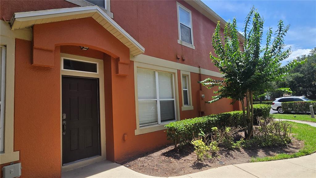 The exterior of a two-story orange stucco townhouse features a dark front door and landscaping — 2921 PINE OAK TRAIL, SANFORD, FL
