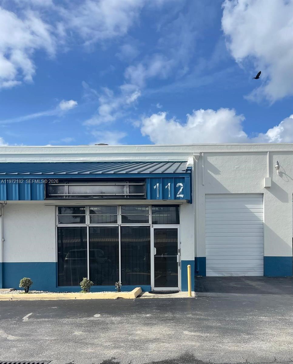 The exterior of a commercial building features a blue metal awning, glass storefront, and garage door — 3100 Milam Dairy Rd # 112, Miami FL 33122, MIAMI, FL