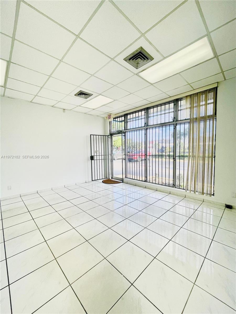 A commercial space features white tiled floors, a drop ceiling, and large windows with security bars — 3100 Milam Dairy Rd # 112, Miami FL 33122, MIAMI, FL