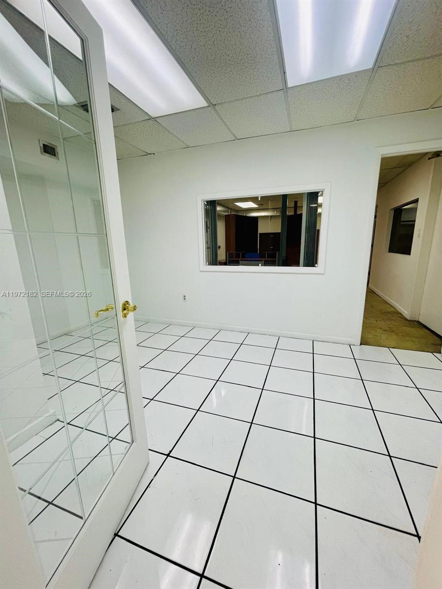 An office room features white tiled flooring, a glass-paned door, and an interior window — 3100 Milam Dairy Rd # 112, Miami FL 33122, MIAMI, FL
