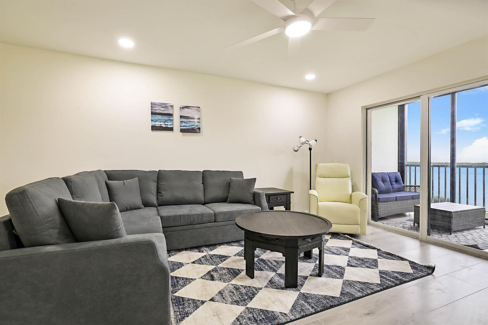 A living room features a gray sectional sofa, a round coffee table, and a balcony view — 300 Intracoastal Place # 203, Jupiter FL 33469, JUPITER, FL