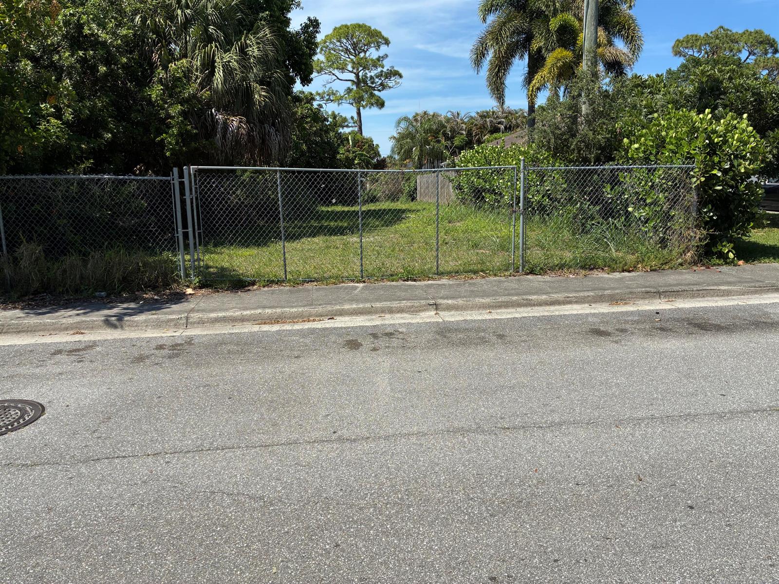 A chain-link fence encloses a vacant, grassy lot bordered by trees and shrubs — 6755 1st Street, Jupiter FL 33458, JUPITER, FL