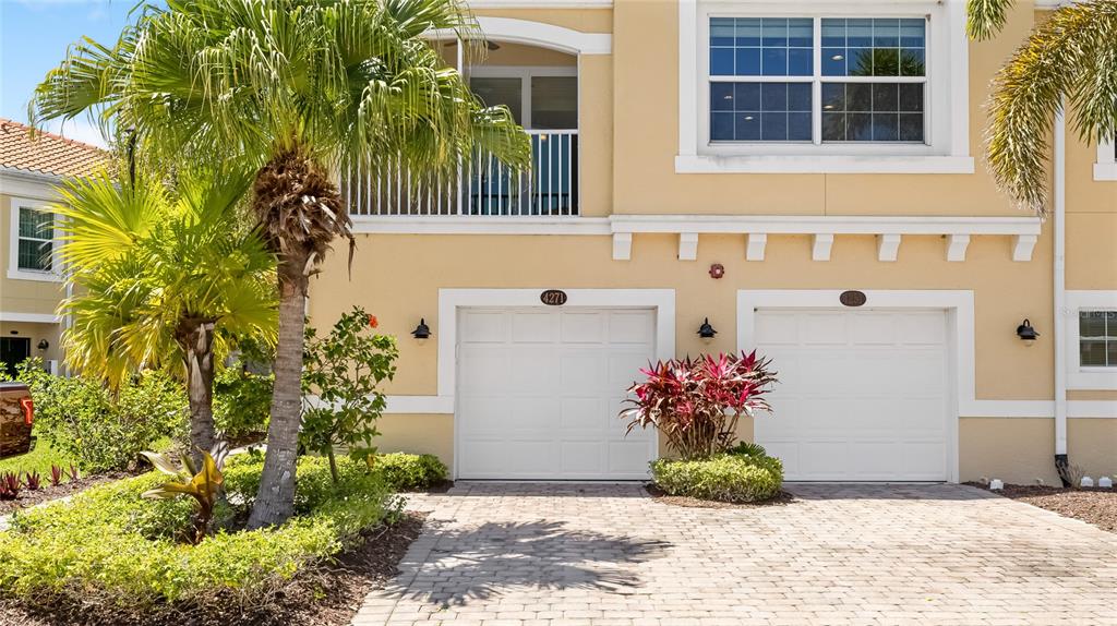 A two-story tan townhouse exterior features two white garage doors and a palm tree — 4271 EXPEDITION WAY UNIT 103, OSPREY, FL