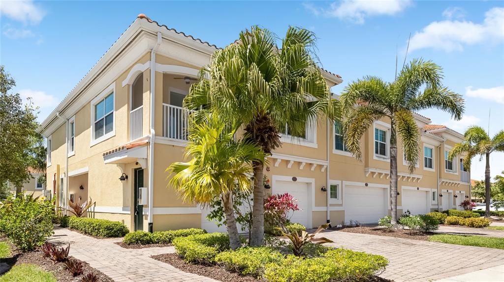 A multi-story tan townhouse with a paved driveway, palm trees, and a second-floor balcony — 4271 EXPEDITION WAY UNIT 103, OSPREY, FL