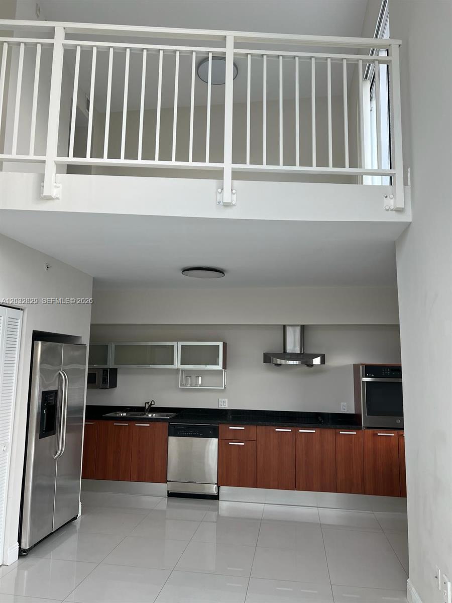 A kitchen with wood cabinets, stainless steel appliances, and a lofted balcony above — 1650 Brickell Ave # 206, Miami FL 33129, MIAMI, FL