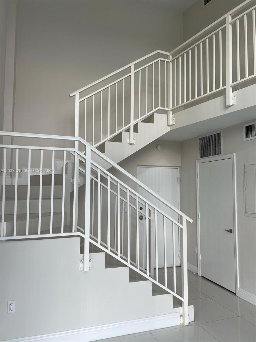 A white staircase with metal railings leads to an upper landing in a tiled room — 1650 Brickell Ave # 206, Miami FL 33129, MIAMI, FL