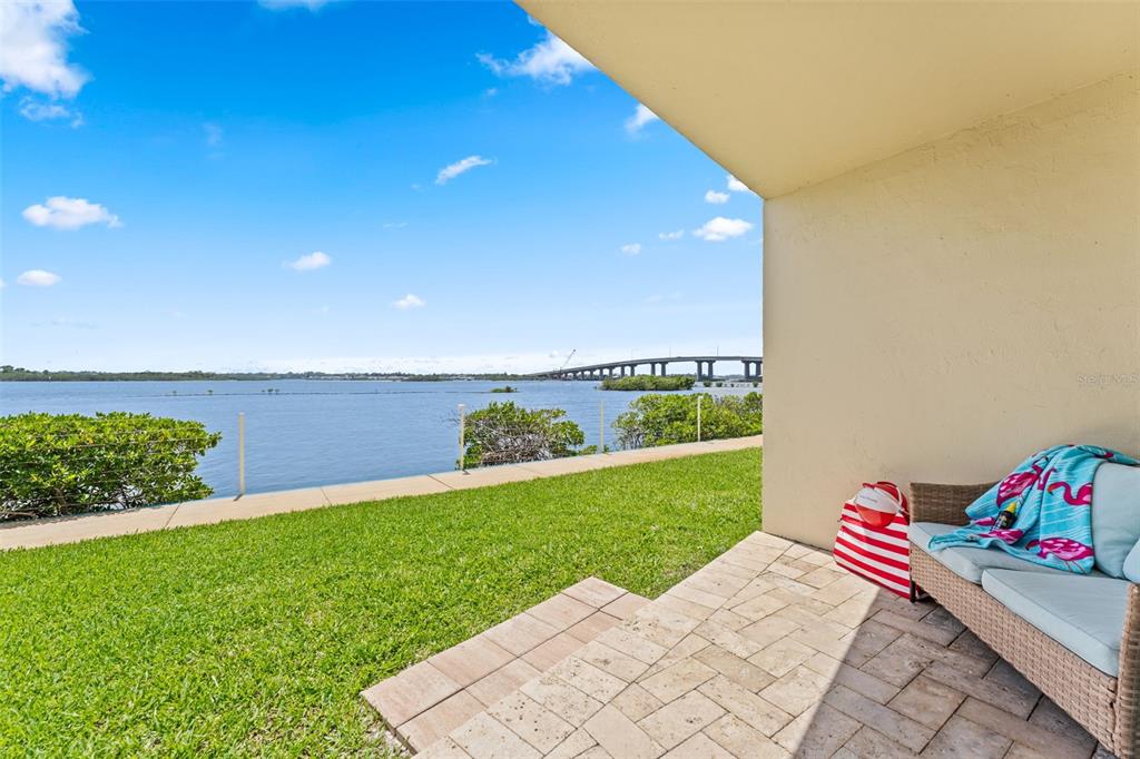 A patio with a wicker sofa overlooks a grassy lawn, a bay, and a bridge — 3606 S PENINSULA DRIVE UNIT 103, PORT ORANGE, FL