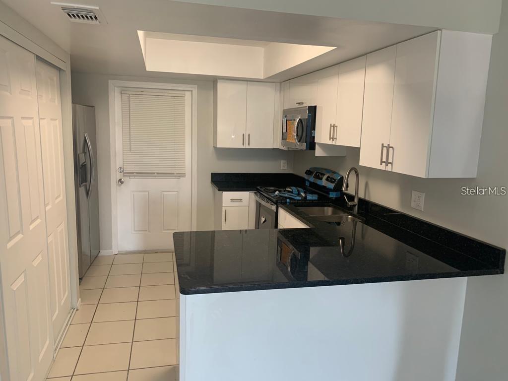 A kitchen features white cabinets, black countertops, stainless steel appliances, and light-colored floor tiles — 49 LAS BRISAS COURT, KISSIMMEE, FL