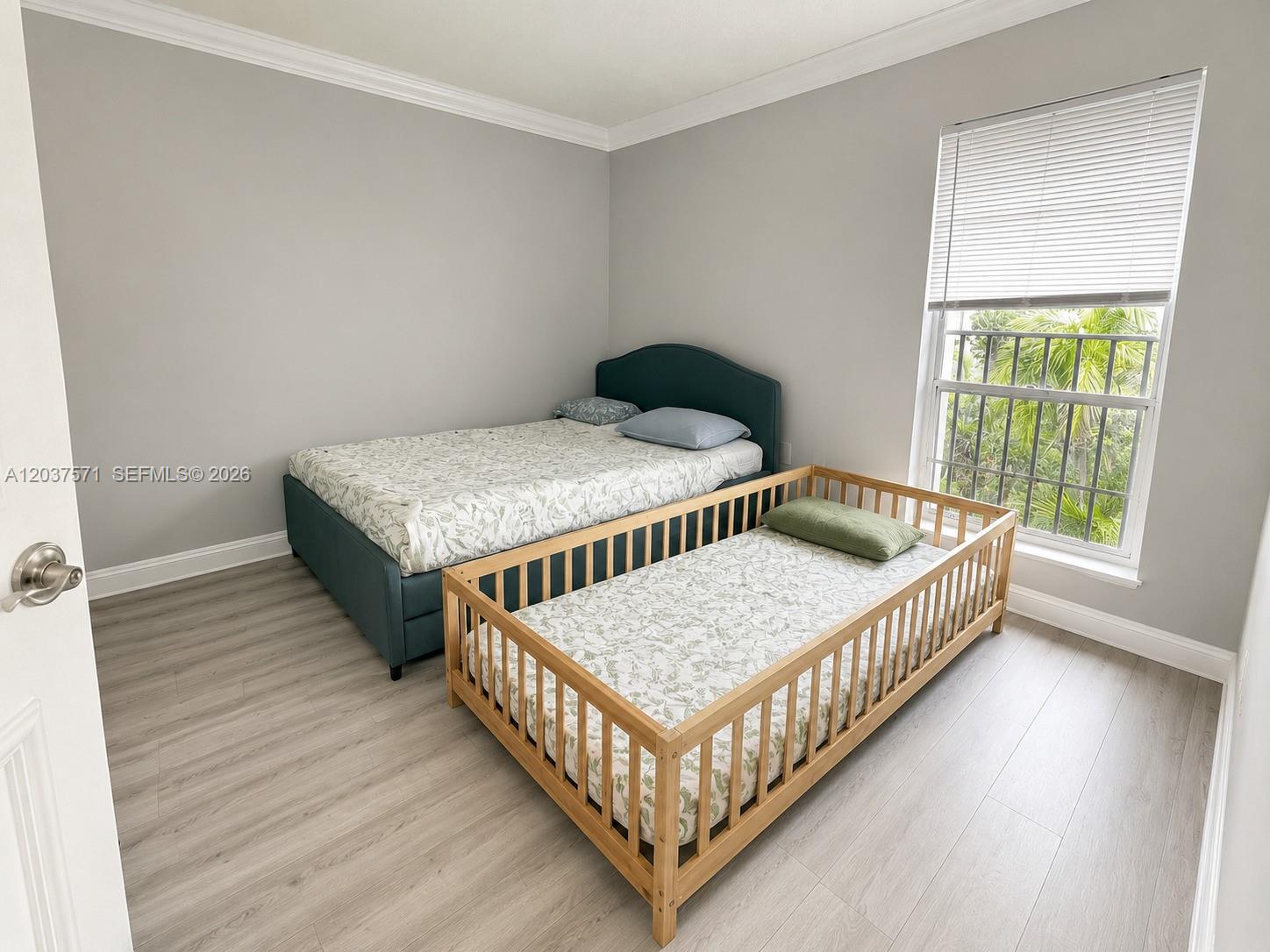 A bedroom features light wood-look flooring, gray walls, a bed, and a wooden toddler bed — 6886 N Kendall Dr # D407, Pinecrest FL 33156, PINECREST, FL
