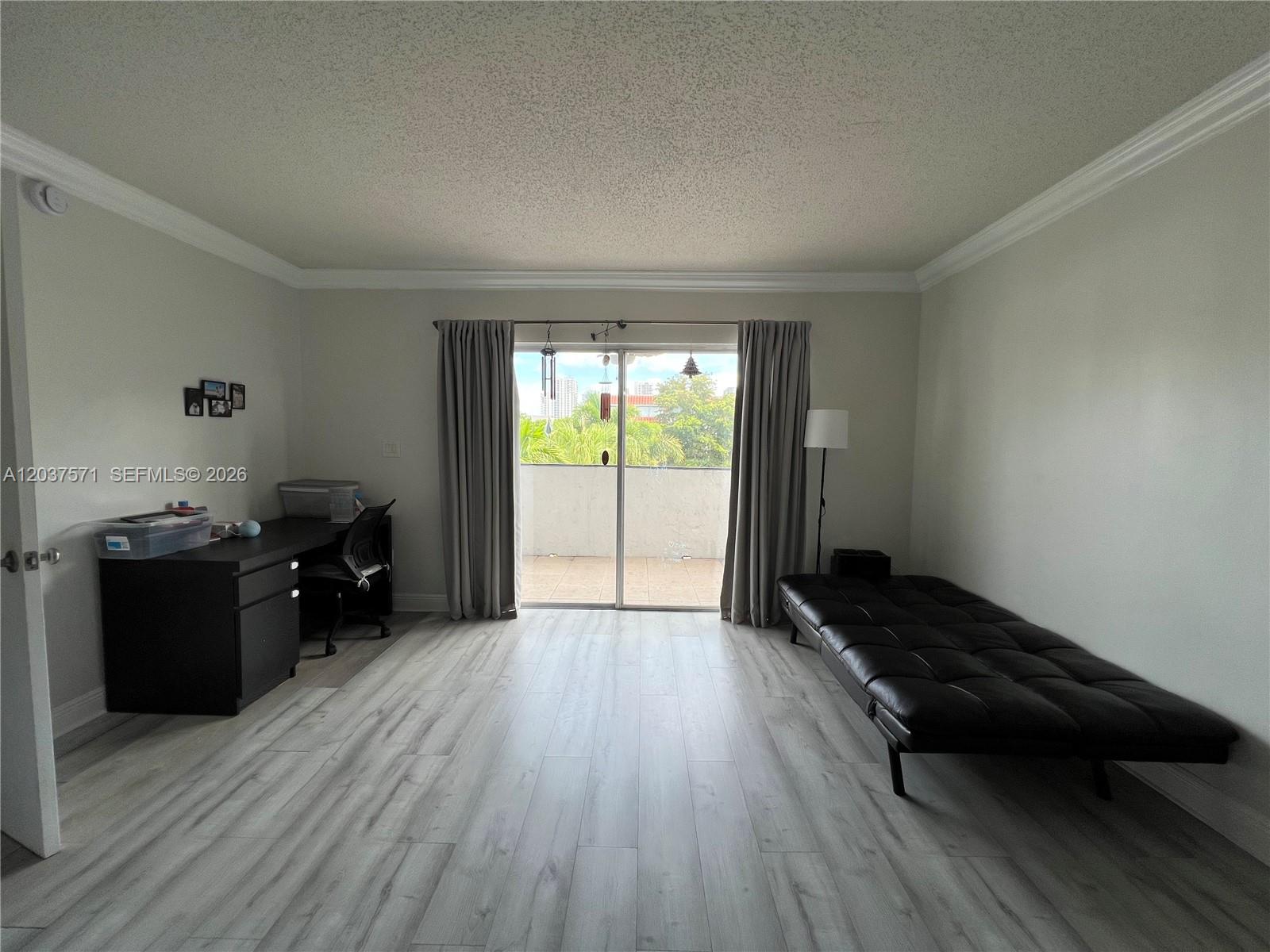 A room with light wood-look flooring, a black desk, a black futon, and a balcony door — 6886 N Kendall Dr # D407, Pinecrest FL 33156, PINECREST, FL