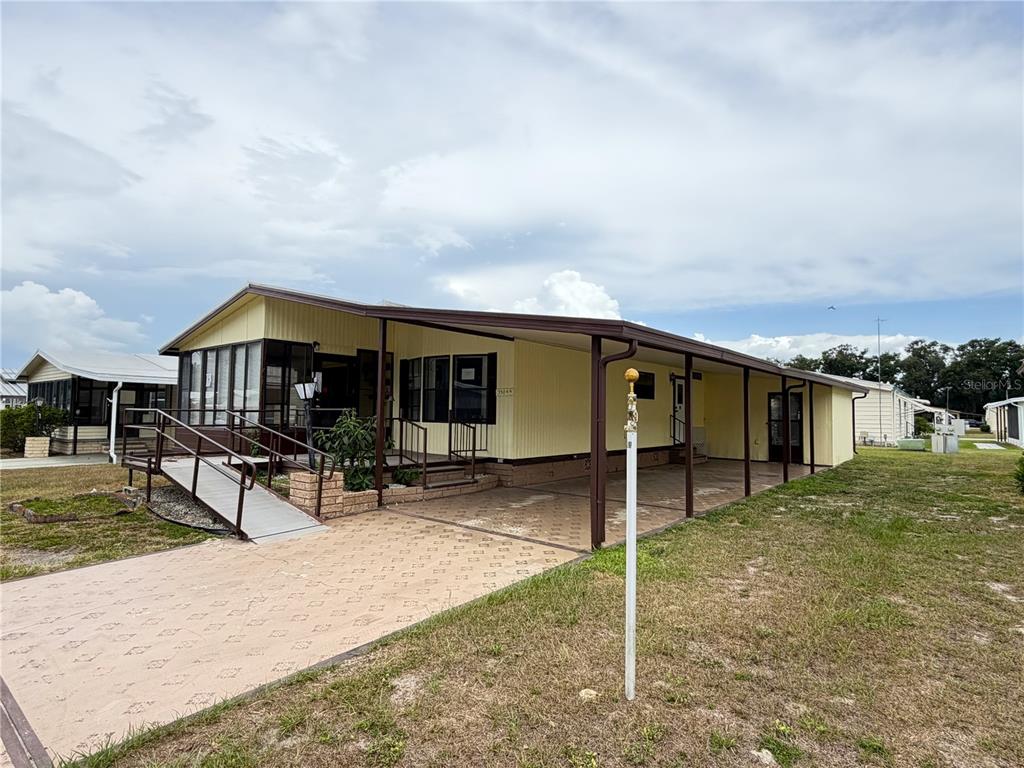 A yellow mobile home features a paved driveway, a covered carport, and a wheelchair ramp — 35044 MCCULLOUGHS LEAP, ZEPHYRHILLS, FL