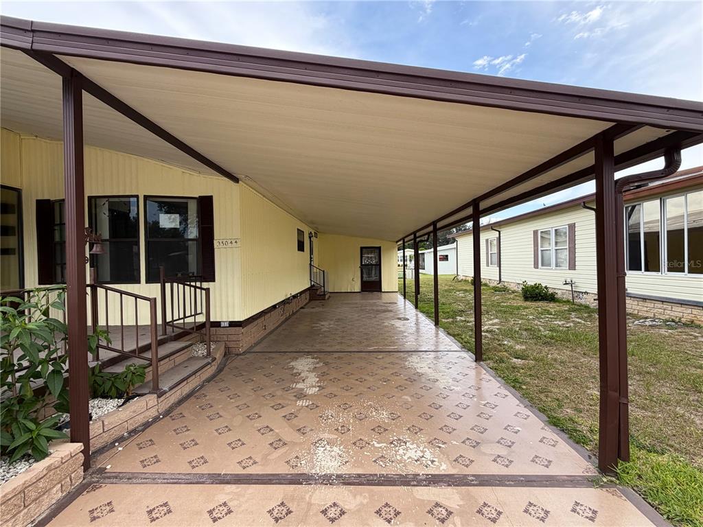 A covered carport with a patterned concrete floor sits beside a yellow mobile home — 35044 MCCULLOUGHS LEAP, ZEPHYRHILLS, FL