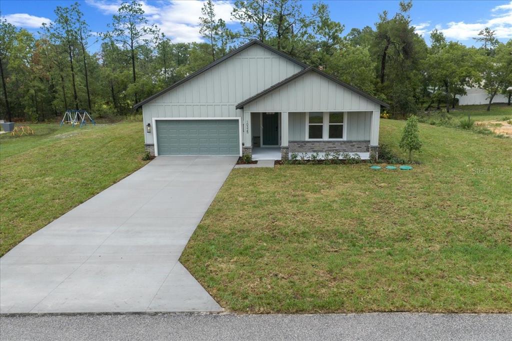 A single-story house with light green vertical siding, a stone base, and a concrete driveway — 10325 DOTTED WREN AVENUE, WEEKI WACHEE, FL