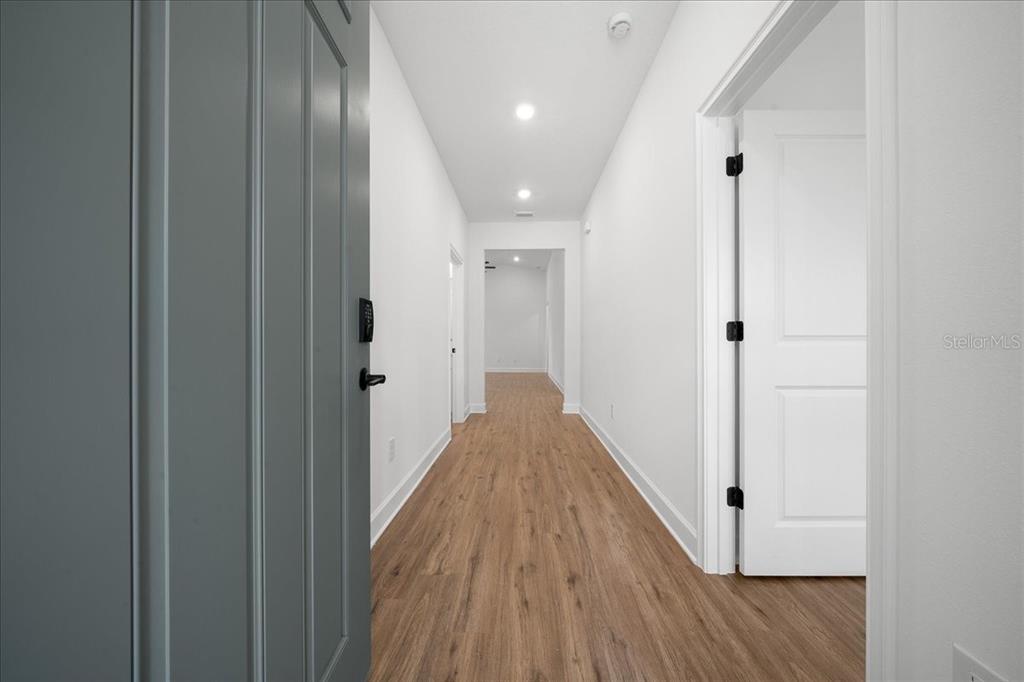 A hallway with light wood-look flooring, white walls, and recessed lighting leads to another room — 10325 DOTTED WREN AVENUE, WEEKI WACHEE, FL