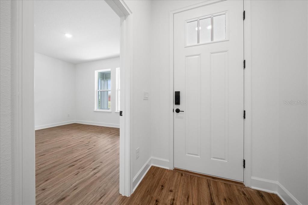 An entryway with wood-look flooring leads to a room with windows and white walls — 10325 DOTTED WREN AVENUE, WEEKI WACHEE, FL