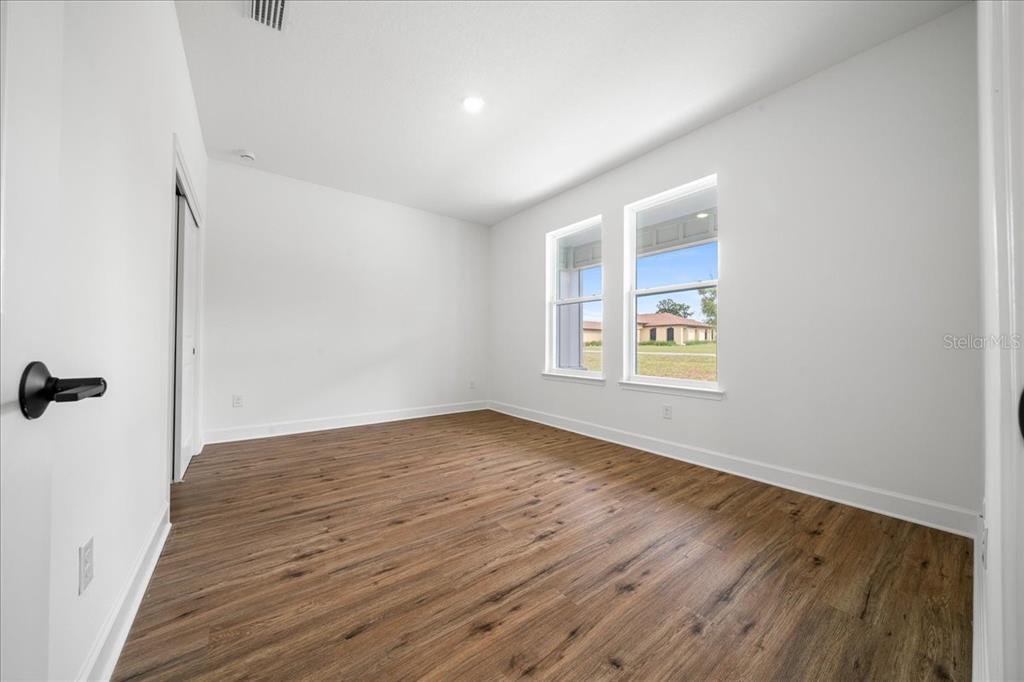 An empty bedroom features white walls, wood-look flooring, and two windows overlooking a neighboring house — 10325 DOTTED WREN AVENUE, WEEKI WACHEE, FL