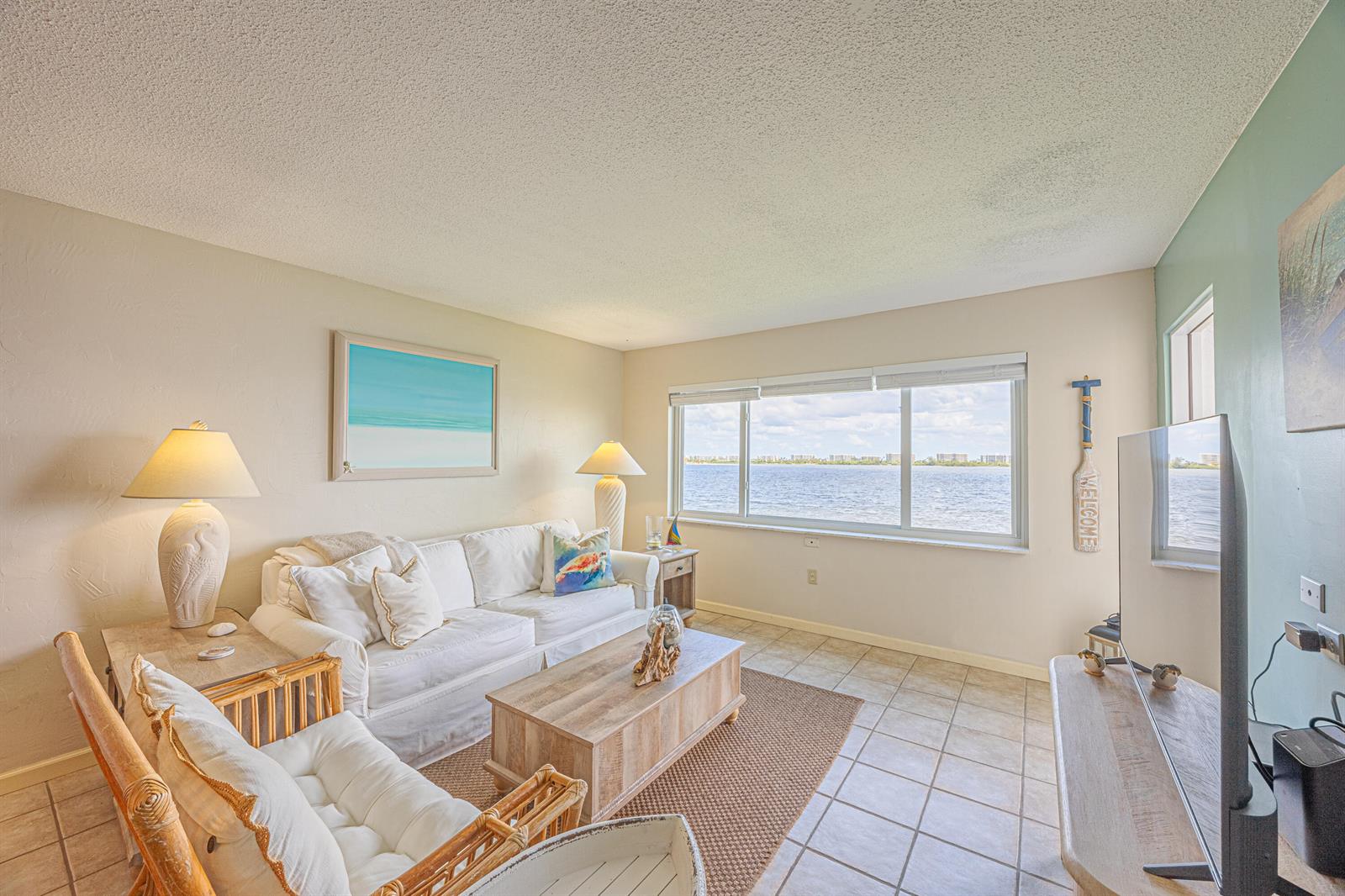 A living room with a white sofa, rattan chair, and a large window overlooking water — 1516 S Lakeside Drive # 203, FL 33460, FL