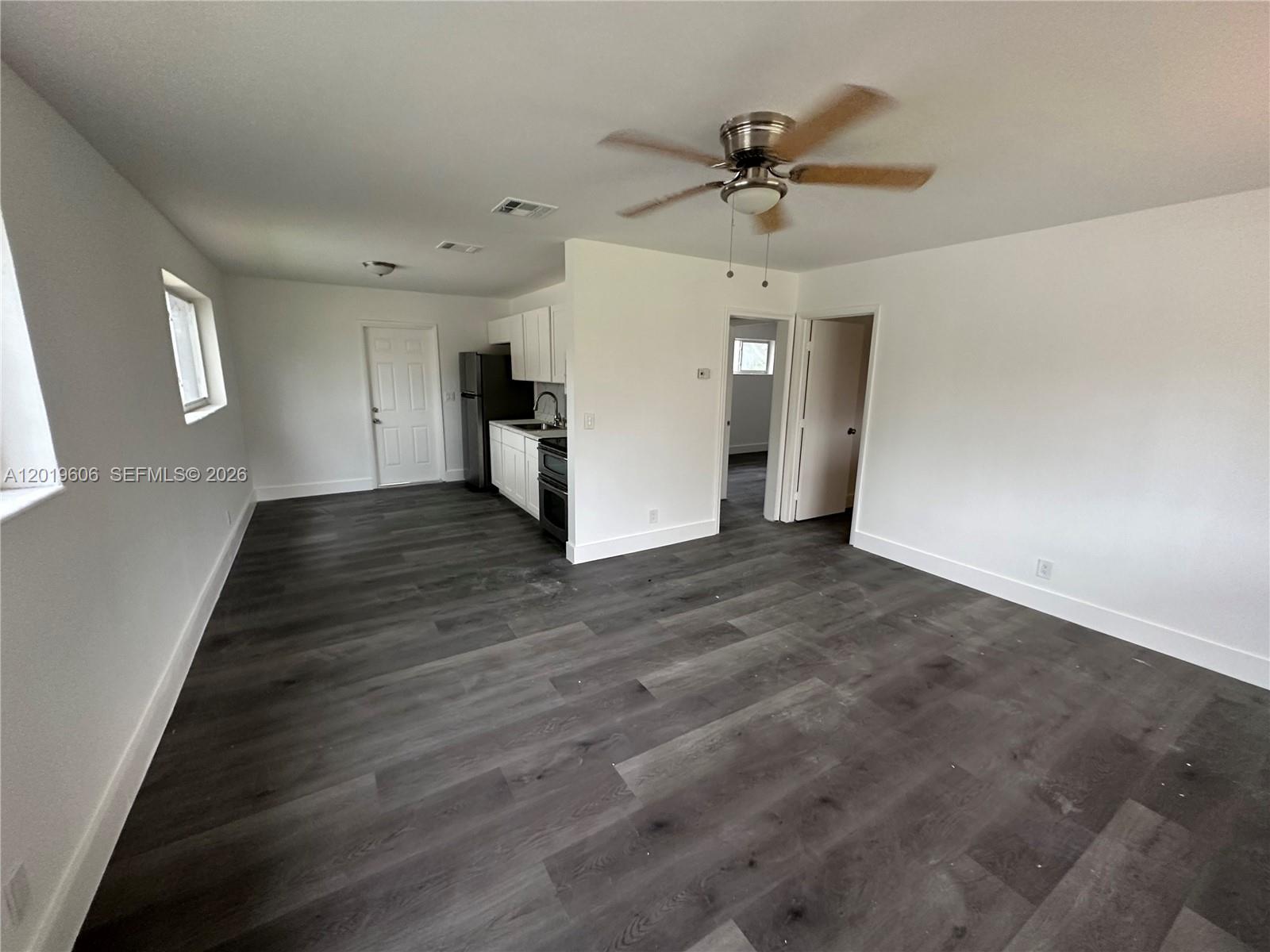 An open-concept living area features white walls, gray wood-look flooring, and a small kitchen — 117 SE 2nd Ave # 1, Hallandale Beach FL 33009, HALLANDALE BEACH, FL