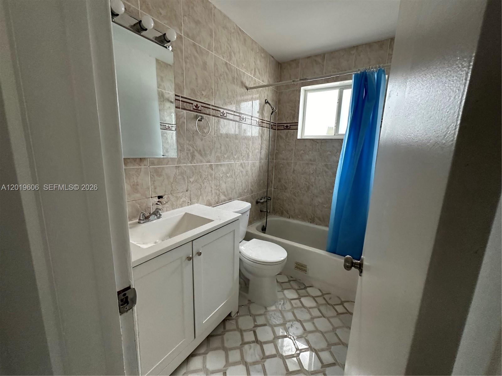 A bathroom features a white vanity, a toilet, and a tiled bathtub with a blue curtain — 117 SE 2nd Ave # 1, Hallandale Beach FL 33009, HALLANDALE BEACH, FL
