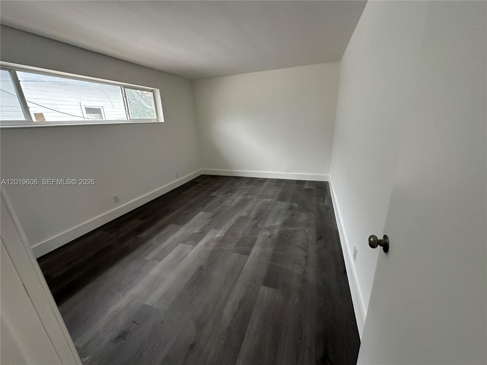 An empty room features white walls, dark wood-look flooring, and a horizontal window — 117 SE 2nd Ave # 1, Hallandale Beach FL 33009, HALLANDALE BEACH, FL